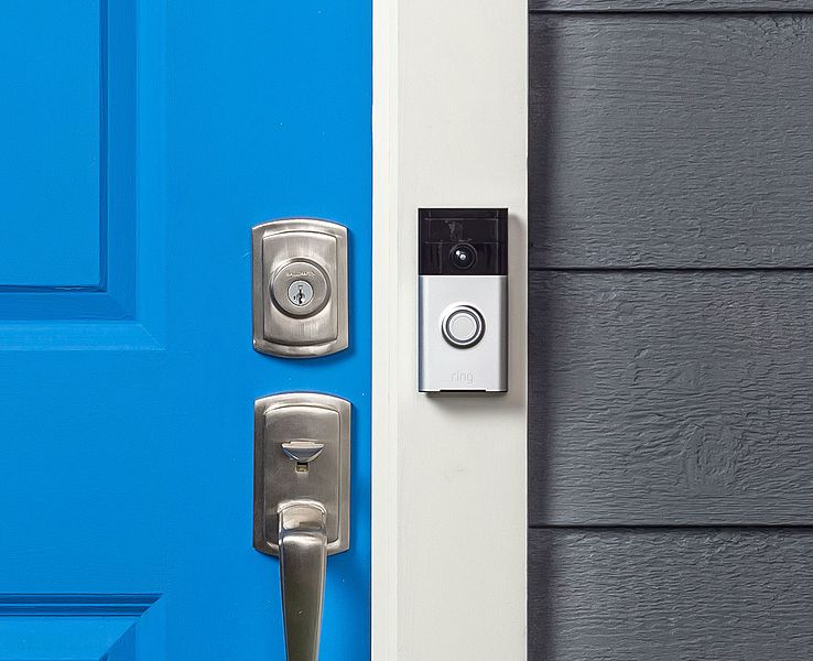 Ring video doorbell attached to white doorframe in between blue door and gray wall